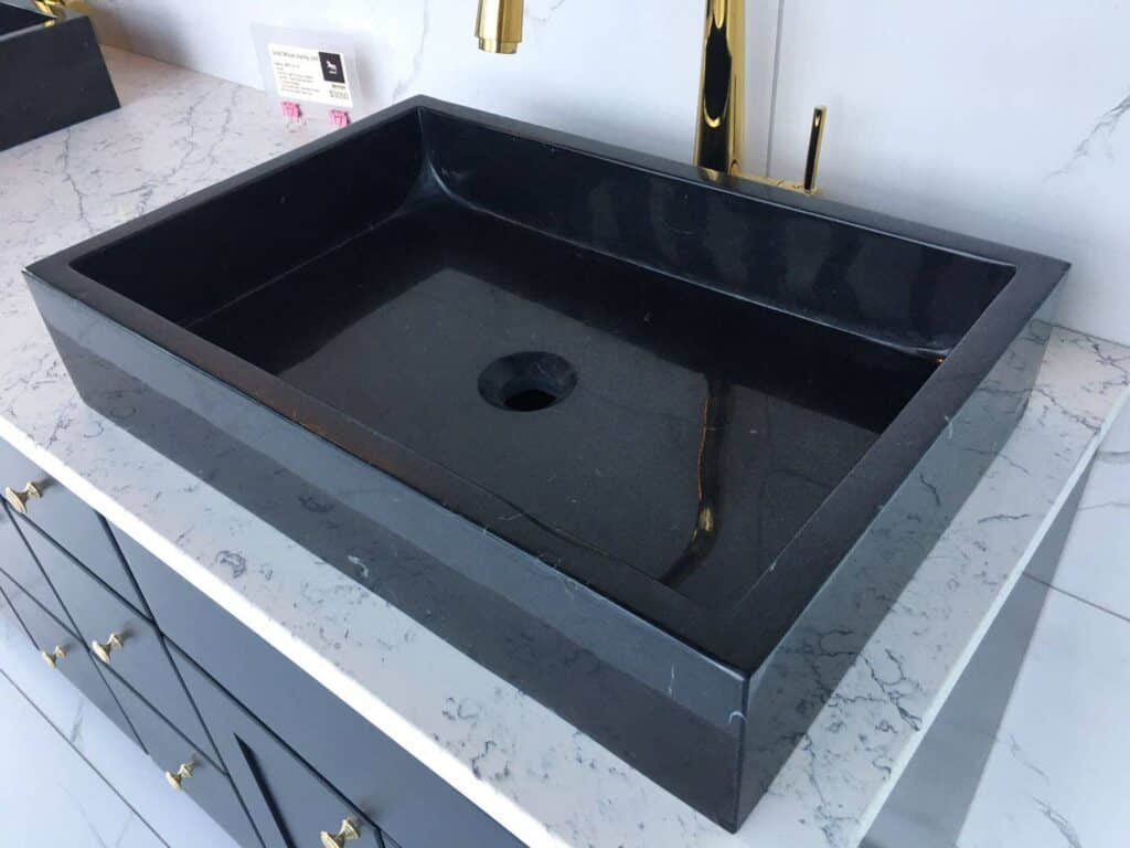 Black rectangular sink on marble countertop with gold faucet.