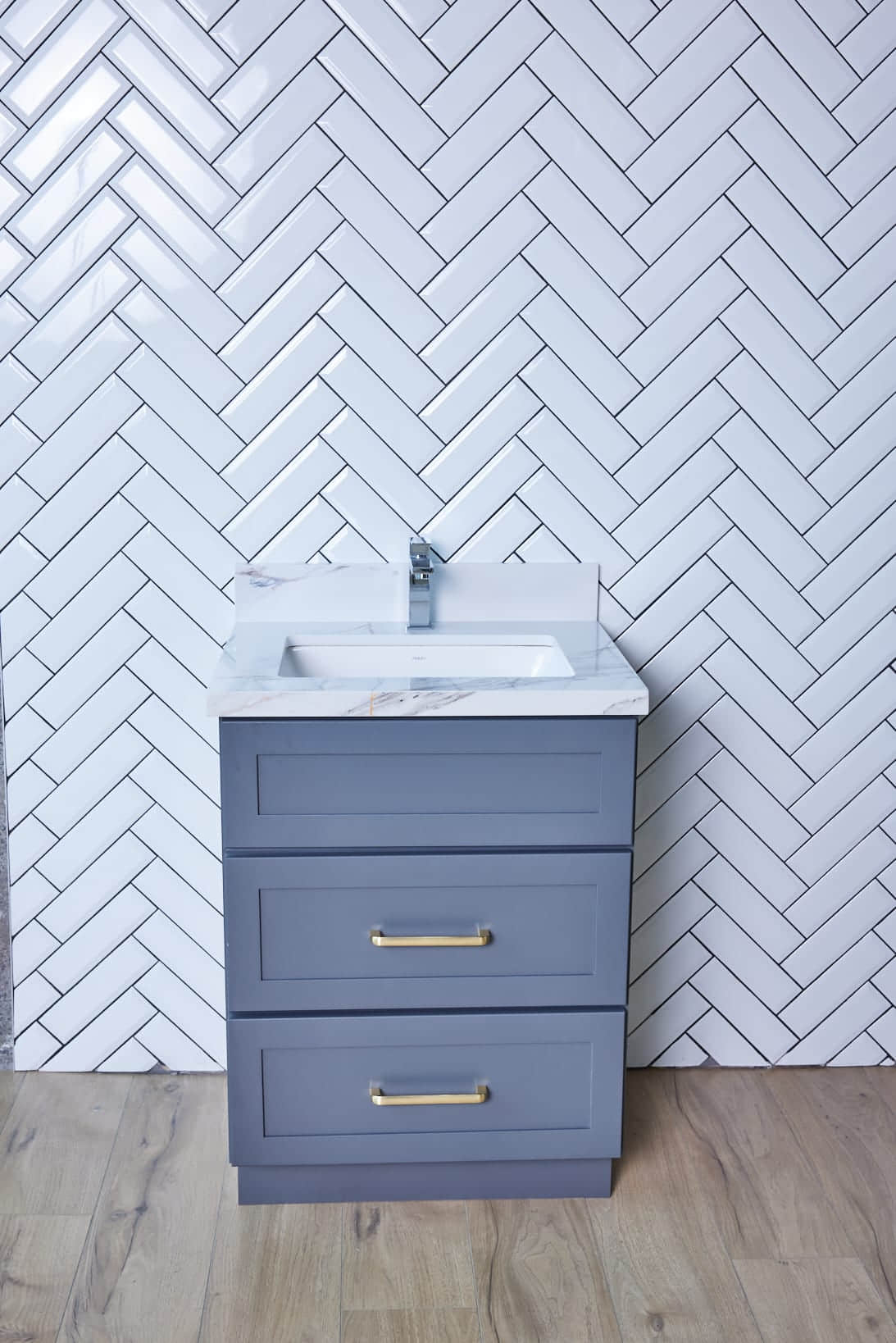 Gray bathroom vanity with herringbone tile backsplash.