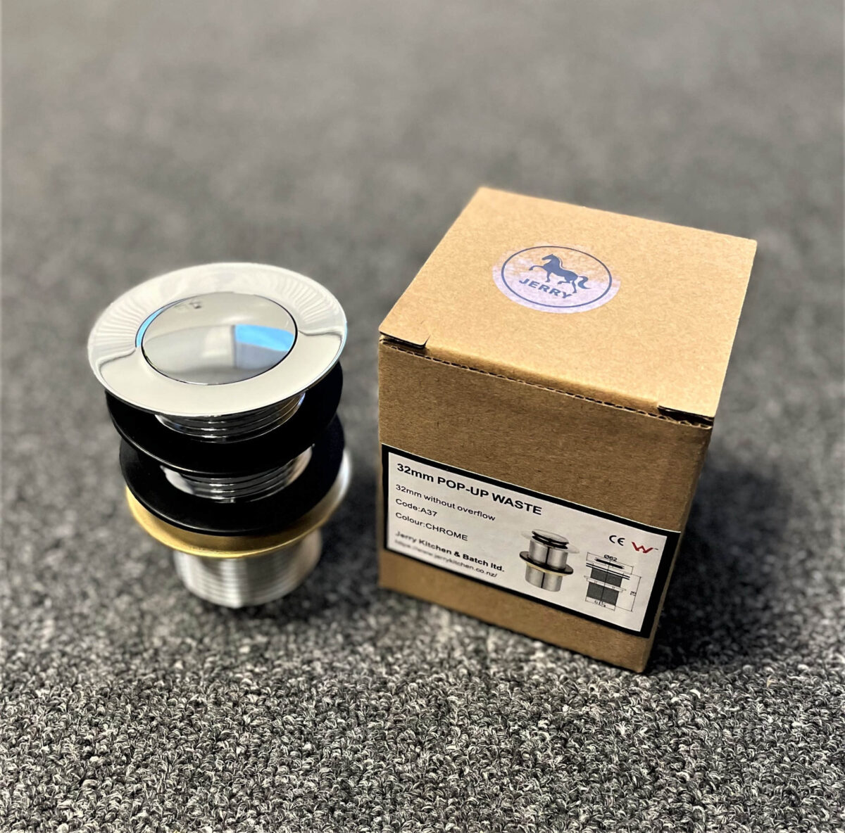 Chrome pop-up waste without overflow next to packaging on carpeted surface.