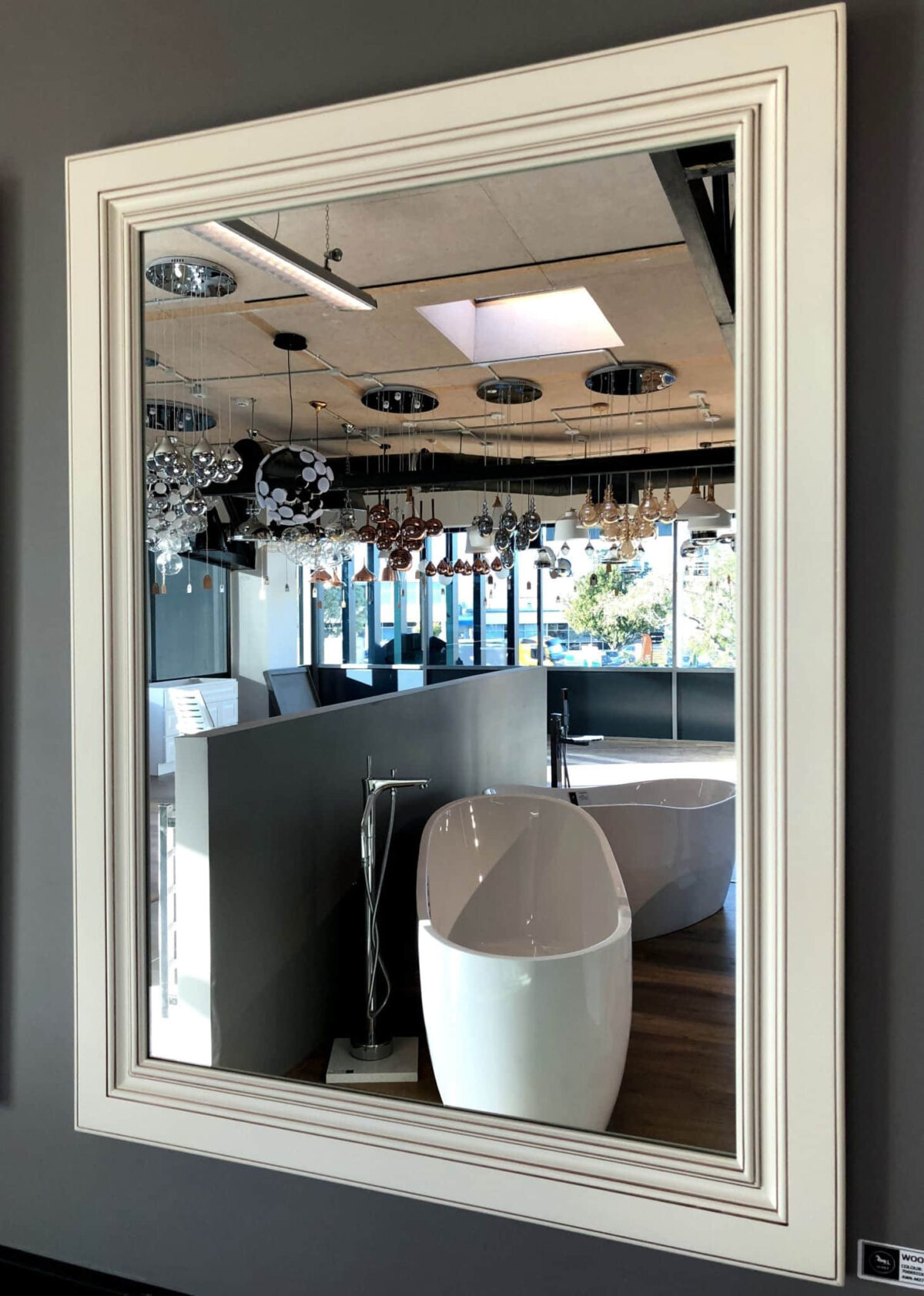 AWK M 2736 Framed mirror reflecting modern bathroom showroom with bathtubs and lighting fixtures.