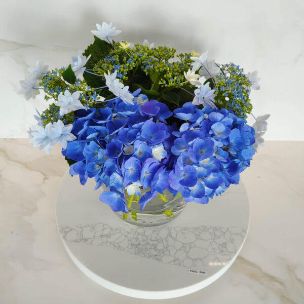 Blue and white hydrangea bouquet in a glass vase on marble surface.
