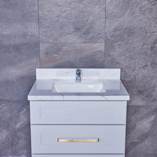 White bathroom vanity with marble countertop and gold handles against gray tile wall.